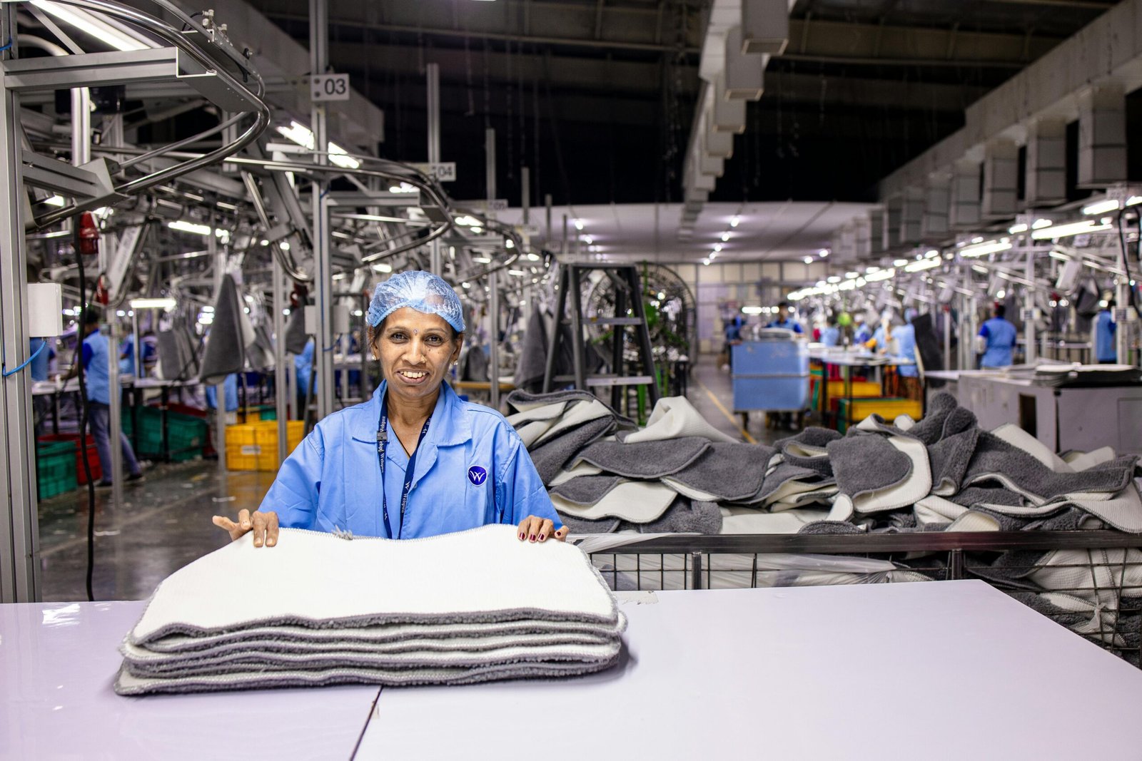 A textile worker in a factory folds products surrounded by industrial machines.